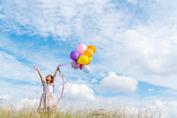 веселая милая девушка, держащая воздушные шары, бегущие по зеленому лугу белого облака и голубого неба со счастьем. руки, держащие яркие воз - sun sky child balloon стоковые фото и изображения