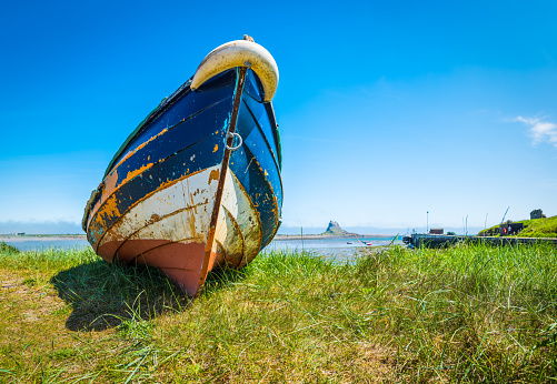Colorfully painted wooden fishing boat pulled onto the grassy shore of Lindisfarne, Northumberland, UK.