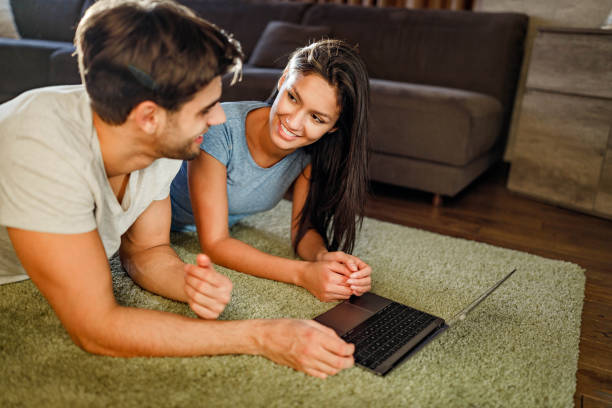 istock Happy couple talking while using laptop on carpet at home. 1326211104
