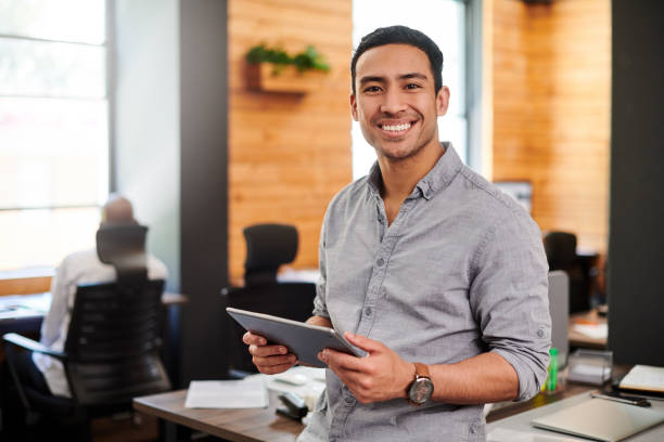 foto de um jovem empresário usando um tablet digital em um escritório moderno - ipad people holding young adult - fotografias e filmes do acervo