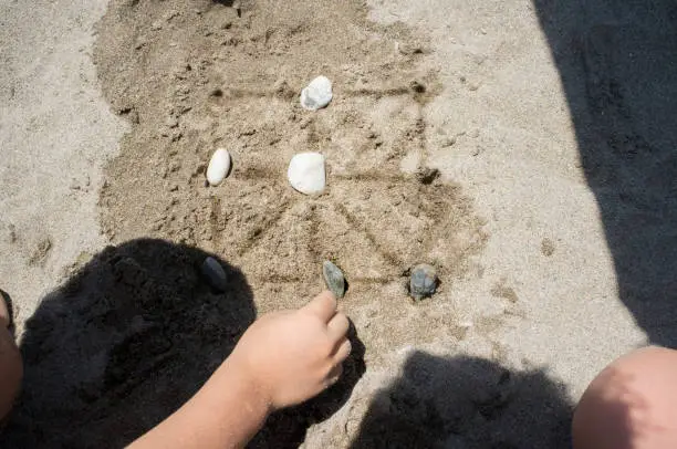 Photo of Children playing tic-tac-toe with natural board made with sand marks and beach pebbles