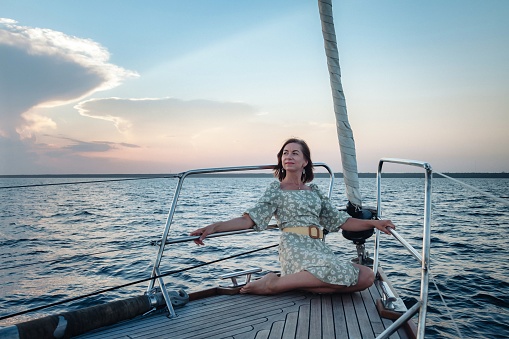 Joyful woman middle age portrait on deck of sailing yacht enjoying water trip on summer coastal cruise. Female businesswoman on sailboat during sunset. Concept travel adventure, yachting and vacation