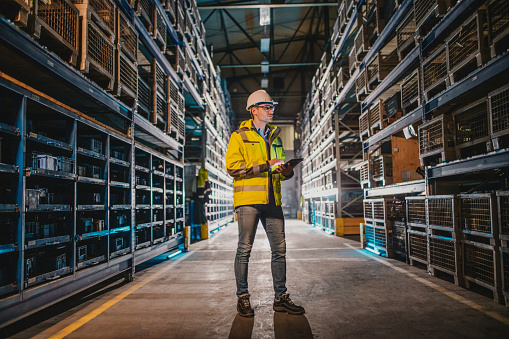 Male factory worker in reflective clothing looking at crate while holding digital tablet.