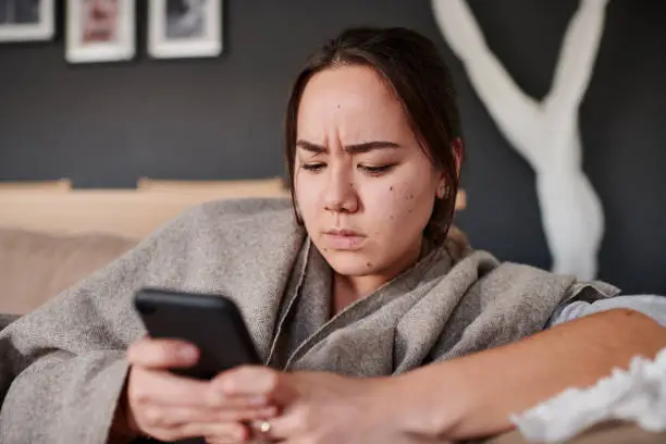 Photo of Shot of a woman looking serious while using her cellphone at home