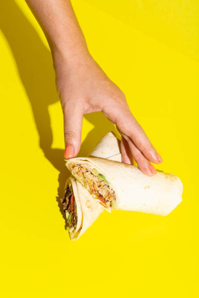 Hand takes doner roll shawarma with chicken and vegetables on yellow stock photo