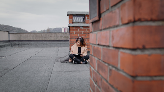 Girl sitting on the roof wearing headphones while writing something