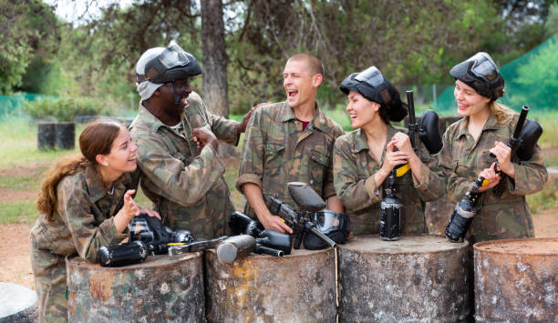 Smiling friends chatting after successful paintball match Group of smiling friends with guns are satisfied by game in paintball outdoors paintballing stock pictures, royalty-free photos & images