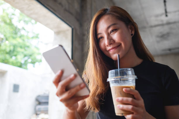 istock a beautiful young asian woman holding and using mobile phone while drinking coffee in cafe 1326222128