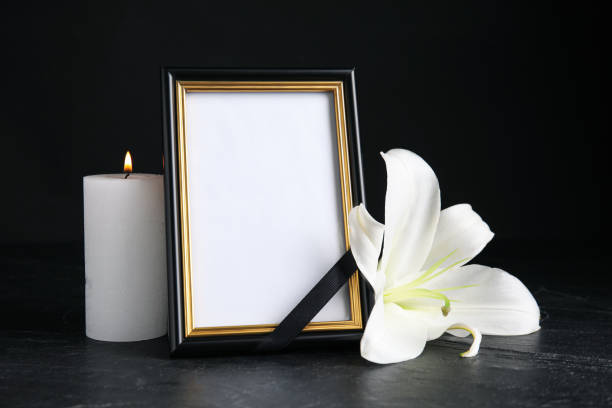 cornice fotografica funebre con nastro, giglio bianco e candela su tavolo nero su sfondo scuro. spazio per il design - necrologio immagine foto e immagini stock