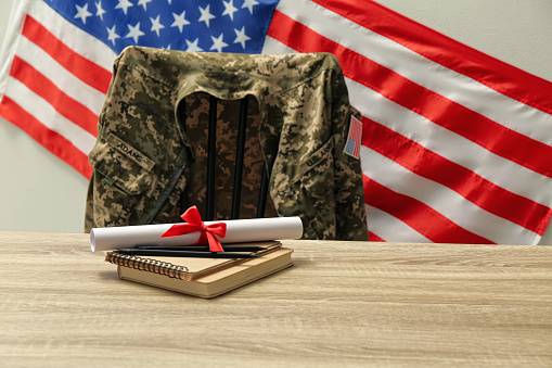 Diploma, notebooks and soldier uniform near flag of United States. Military education