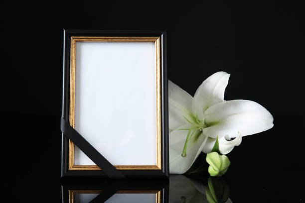 cornice fotografica funebre con nastro e giglio bianco su tavolo nero su sfondo scuro. spazio per il design - necrologio immagine foto e immagini stock