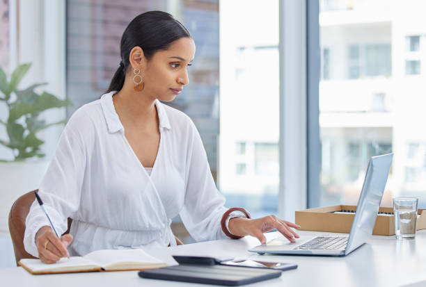 istock Shot of a businesswoman using a laptop in a modern office and making notes in a notebook 1326225772