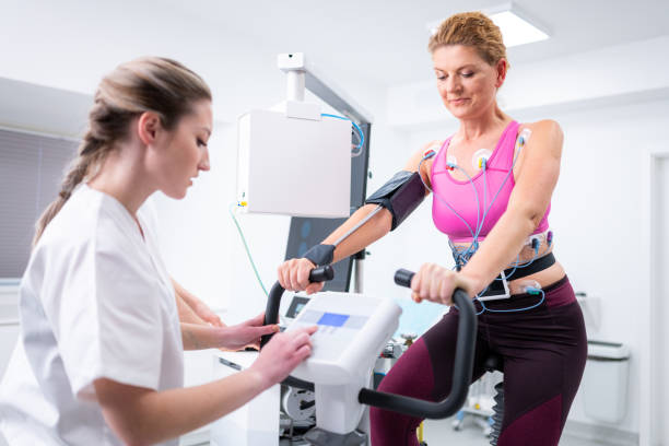 Mature woman taking a cardiopulmonary stress test in clinic Female doctor observing the progress of a cardiopulmonary stress test taken by the mature woman riding a bicycle ergometer. stress test stock pictures, royalty-free photos & images