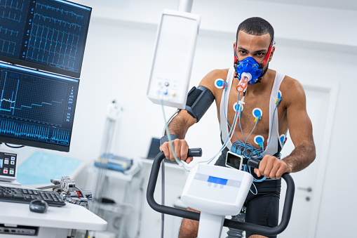 Portrait of male athlete cycling on the ergometer and doing a cardiopulmonary test in clinic.