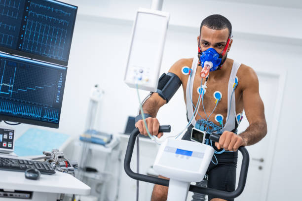 Male athlete taking a cardiopulmonary stress test in clinic Portrait of male athlete cycling on the ergometer and doing a cardiopulmonary test in clinic. stress test stock pictures, royalty-free photos & images