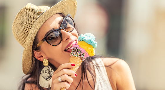 Beautiful happy woman licks ice cream during a hot summer day.