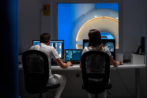 dois radiologistas de ressonância magnética sentados na sala de controle e operando o scanner de ressonância magnética - neuroscience mri scan brain brain surgery - fotografias e filmes do acervo