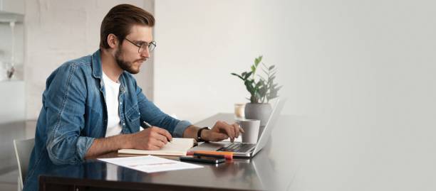 istock Happy young man sitting in home office and using laptop computer, smiling, chatting online 1326233423