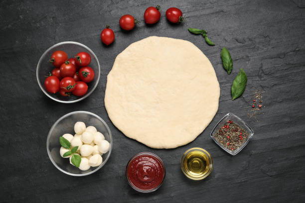 istock Raw dough and other ingredients for pizza on black table, flat lay 1326235343