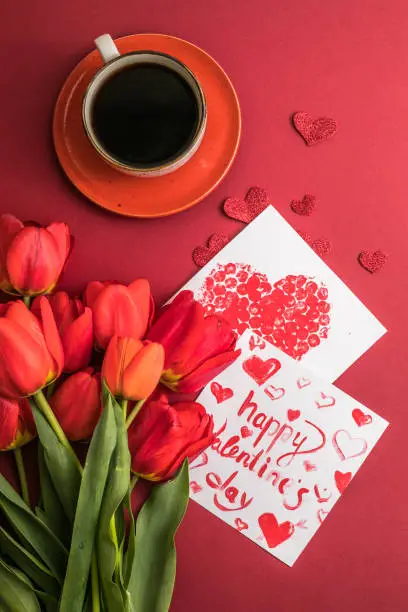 Photo of morning coffee and a bouquet of red tulips on a bright red background. View from above.Copy space for text. The concept of holidays.