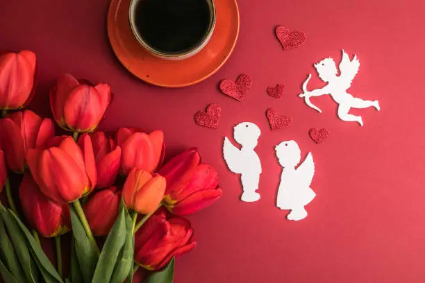 Photo of morning coffee and a bouquet of red tulips on a bright red background. View from above.Copy space for text. The concept of holidays.