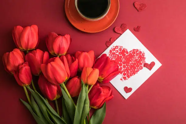 Photo of morning coffee and a bouquet of red tulips on a bright red background. View from above.Copy space for text. The concept of holidays.