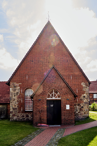 Red brick church with small porch in a village in Lower Saxony, Germany. Backlight shot with sun rays and light reflections overlaid.