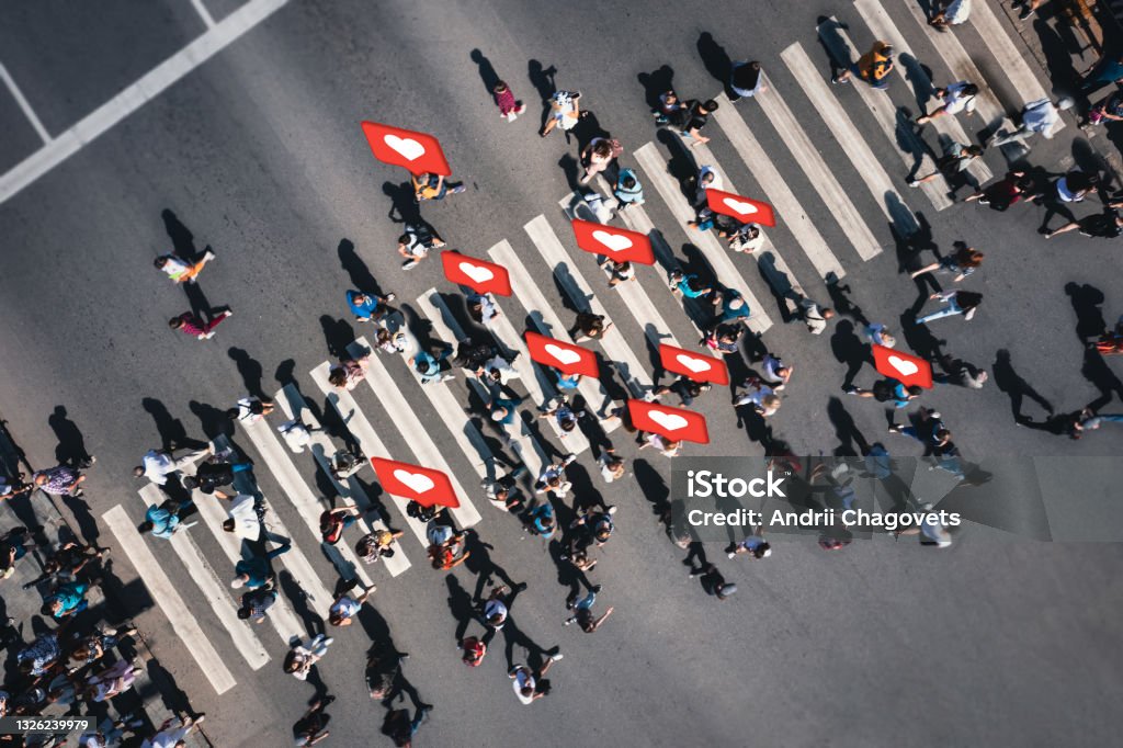 Crowd of people at pedestrian crossing with social heart icons and likes - overhead shot Different people at a pedestrian crossing with social heart icons and likes in the city. People at a zebra pedestrian crossing - a lot of pedestrians in an overcrowded city on a sunny day. Social Issues Stock Photo