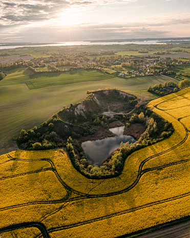 Drone’s eye view of an old sand and gravel quarry on the island of Moen in Denmark surrounded by a field of canola or oilseed rape growing in Denmark. \nColour, vertical  format with some copy space.