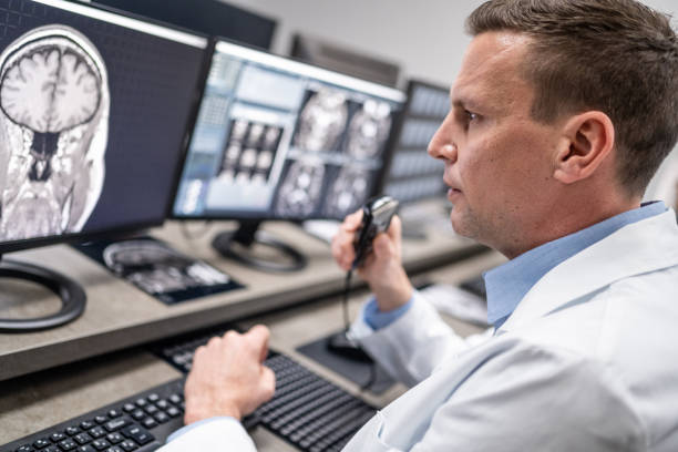 istock Male radiologist speaking into a dictation recorder while looking at MRI scan 1326240286