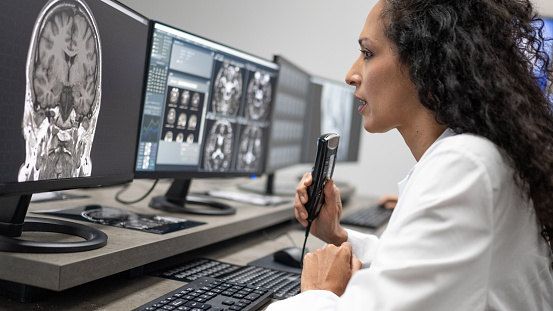 Side view of female radiologist talking into the dictation recorder while looking at the MRI scans on her computer.