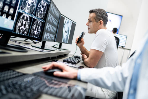 Male radiologist speaking into a dictation recorder while looking at MRI scan