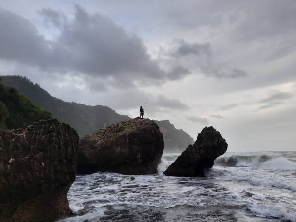 istock A fisherman sitting on a rock formation while big long waves flowing. 1326241246