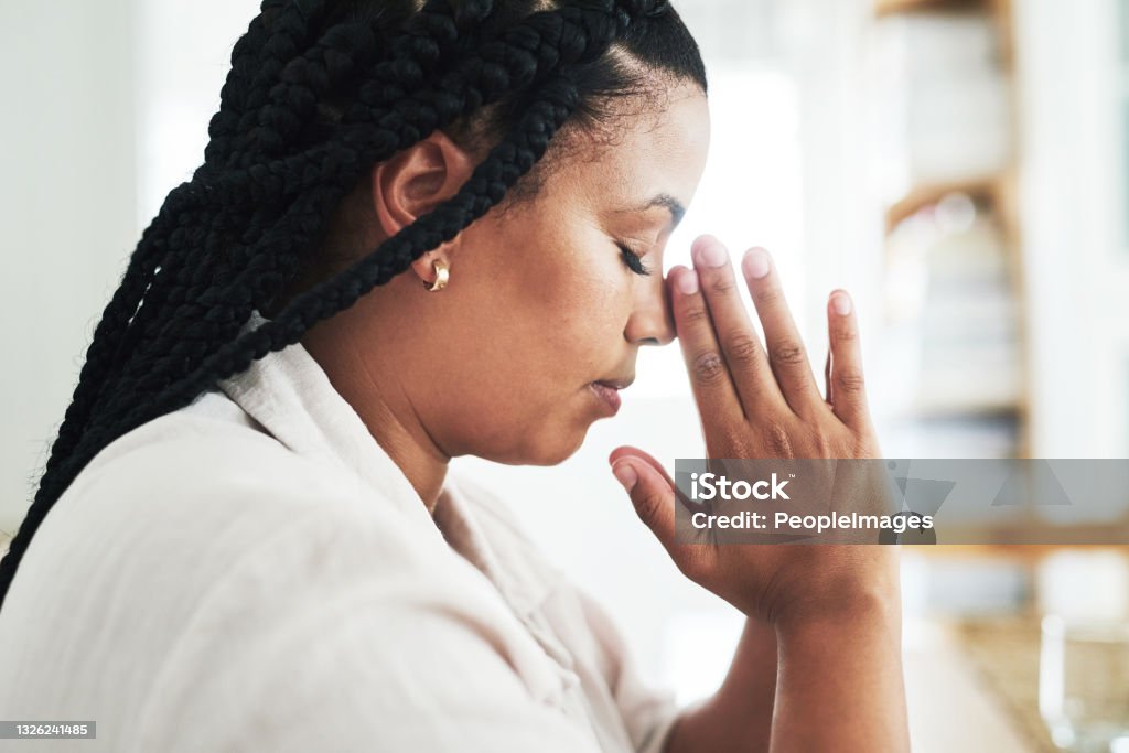Shot of a young woman praying at home True prayer is a way of life Praying Stock Photo