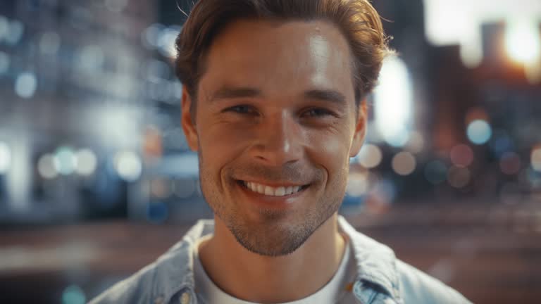 Portrait of a Happy Handsome Young Man in Casual Clothes Standing on the Street at Sunset. Stylish Male Model in Big City Living the Urban Lifestyle. Background with Office Buildings and Billboards.