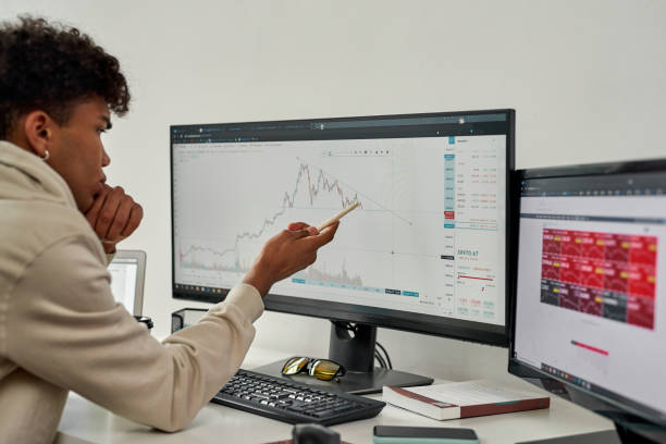 Focused young male trader looking at computer screen, studying charts while trading from home stock photo