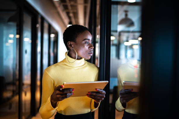 junge geschäftsfrau mit digitalem tablet und wegblick in einem büro - businesswoman business women african descent stock-fotos und bilder
