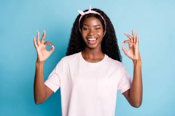 Portrait of charming cheerful wavy-haired brunette girl showing double ok-sign winking isolated over blue pastel color background