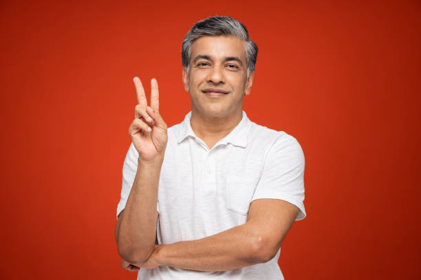 Portrait of mature man standing isolated over red background:- stock photo India, 40-49 Years, Adult, Adults Only, mature men man showing peace sign stock pictures, royalty-free photos & images