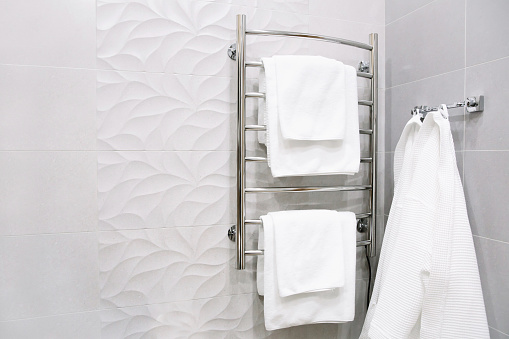 White towels and a bathrobe hang in the bathroom. Bathroom interior in a hotel room, apartments. Heated towel rail in bathroom.
