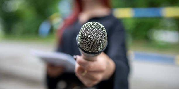 istock Journalist at news conference, writing notes, holding microphones 1326261235