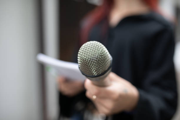 istock Journalist at news conference, writing notes, holding microphones 1326261320