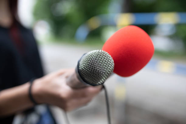 istock Journalist at news conference, writing notes, holding microphones 1326261372