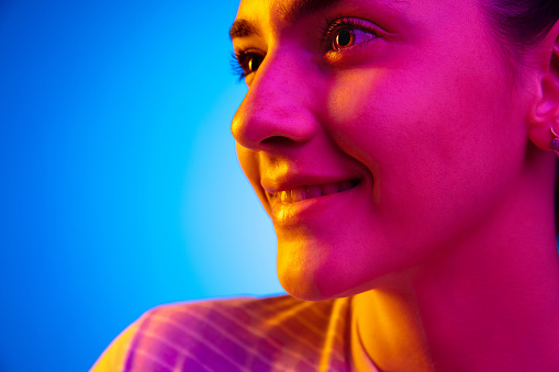 Smiling. Caucasian happy young woman's portrait on dark studio background in neon light. Female model in casual style. Concept of human emotions, facial expression, youth, sales. Copy space for ad.