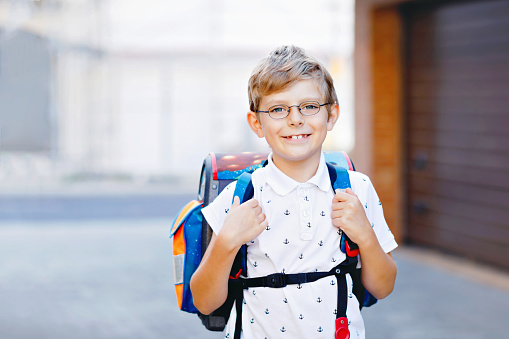 Happy little kid boy with glasses and backpack or satchel. Schoolkid on the way to school. Portrait of healthy adorable child outdoors. Student, pupil, back to school. Elementary school age.