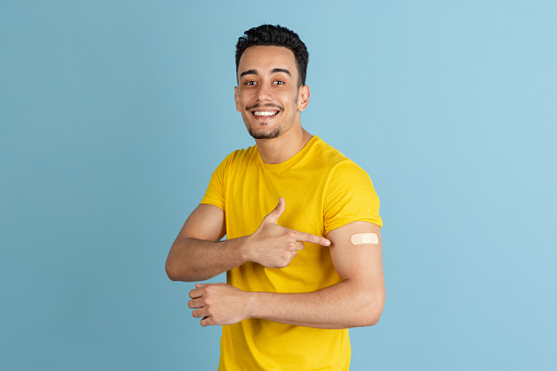 Showing vaccined hand. Caucasian man's portrait isolated on blue studio background, flyer with copyspace for ad. Concept of human emotions, vaccination, healthcare, COVID prevention.