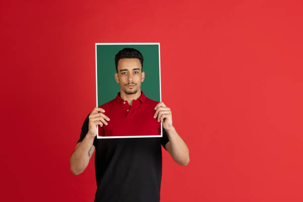 istock Young man holding his portraits isolated over red studio background with copyspace for ad. 1326268814