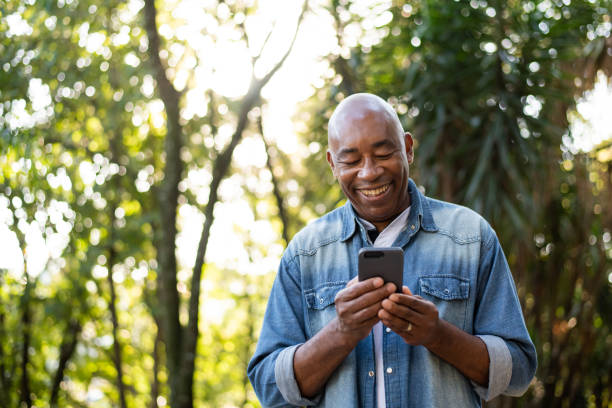 homem de meia-idade sorrindo e usando celular. - mature men - fotografias e filmes do acervo