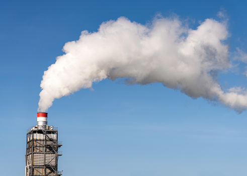 A modern factory's large chimney emitting clouds of effluent into a clear blue sky.