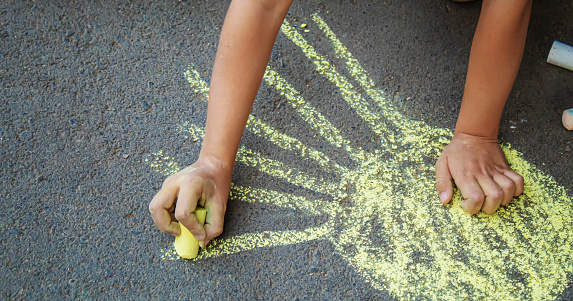 The boy draws with chalk on the pavement the sun.